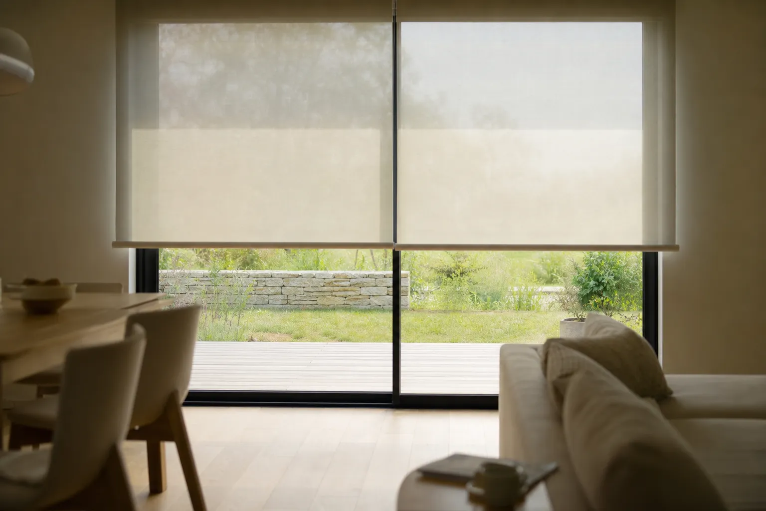 Store intérieur textile descendu à mi-hauteur devant une baie vitrée, lumière filtrée