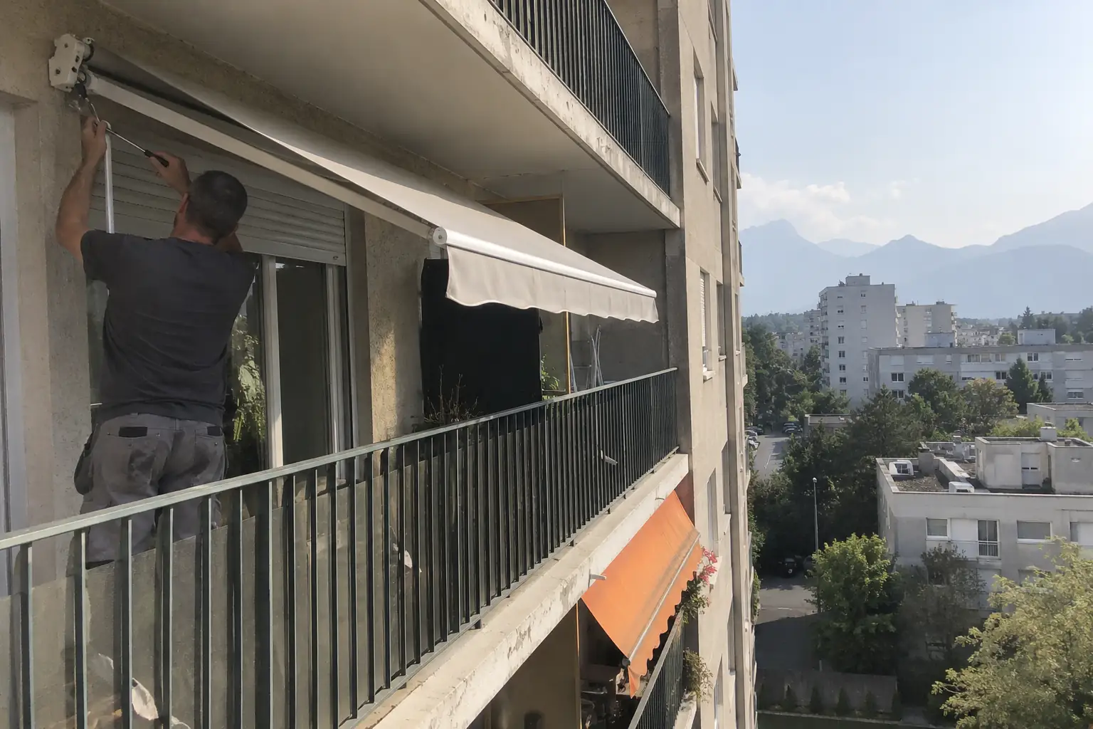 Poseur réglant la toile d’un store banne sur le balcon d’un immeuble, toile rayée orange chez le voisin du dessous